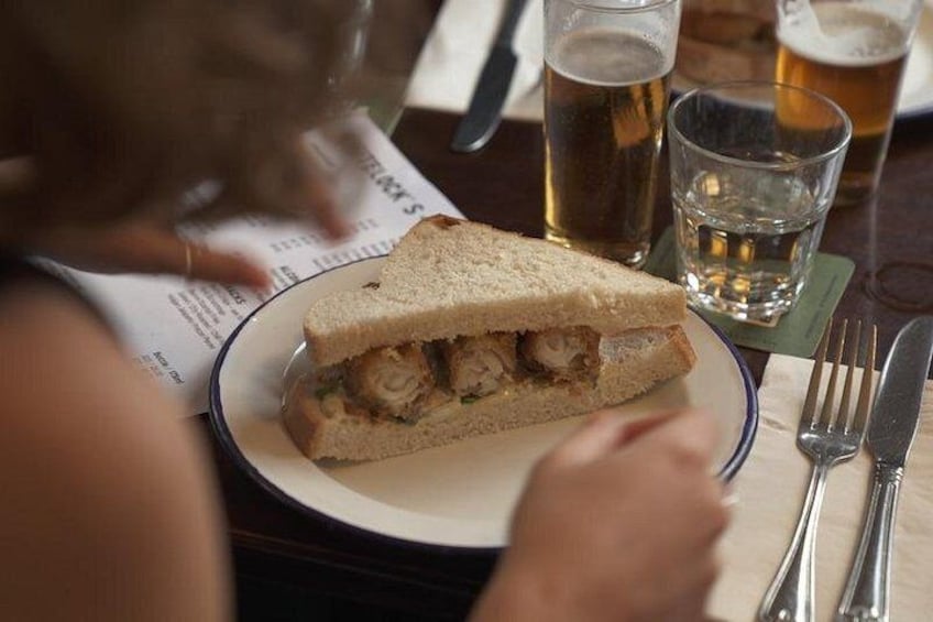 Ein Sandwich auf einem Teller, ein Bierglas und Besteck auf einem Tisch. 2