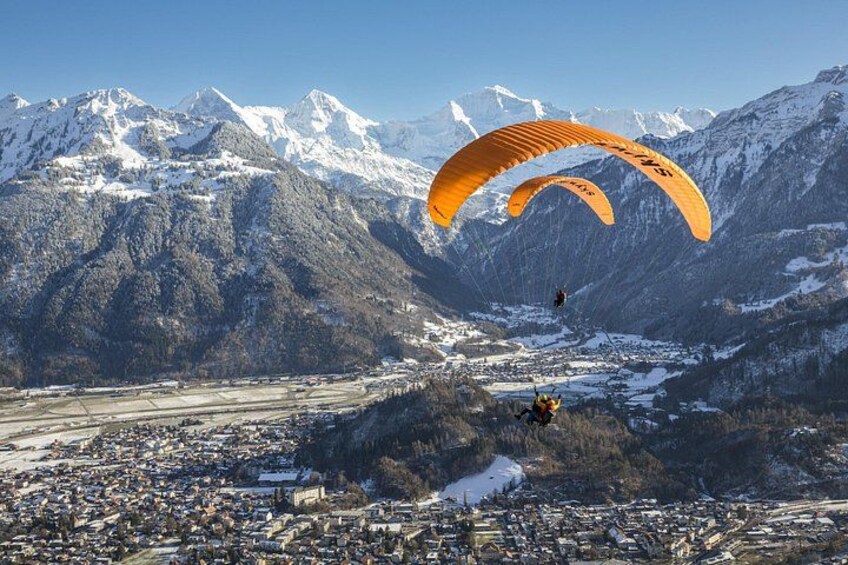 A person paragliding over a mountainous landscape with snow-capped peaks and a town below. 2