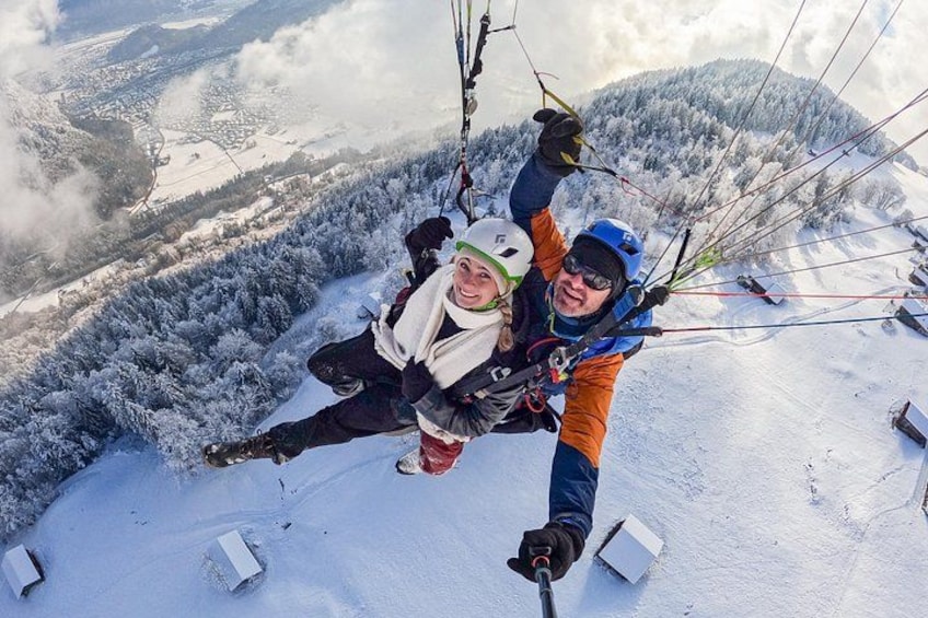 Two people paragliding over a snowy landscape with trees and mountains in the background. 5