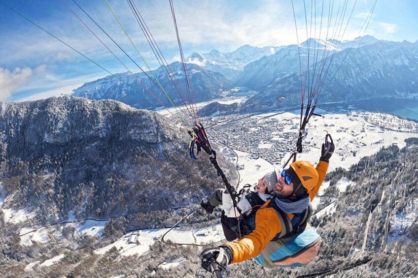 A person paragliding over a mountainous landscape with snow-covered peaks and a town below. 3