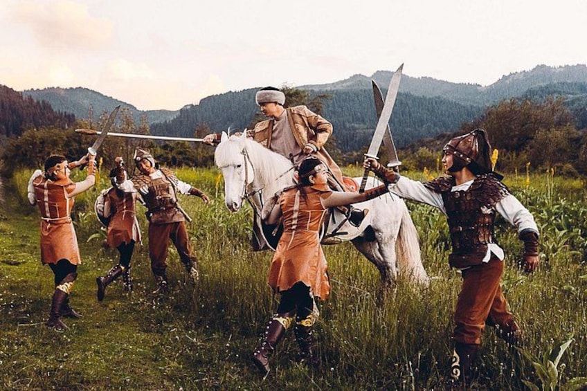 A group of people in historical costumes in a grassy field with mountains in the background. 2