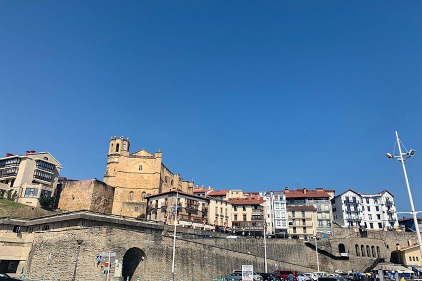 Un paysage urbain historique, avec une imposante structure rappelant un château, des bâtiments modernes et un ciel d’un bleu éclatant. 4