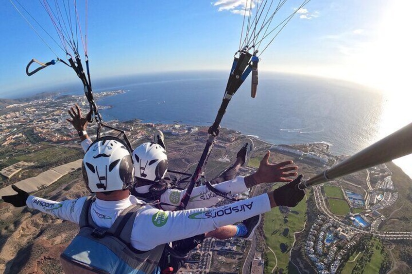 Zwei Gleitschirmflieger mit Helmen und Fallschirmen über einer Küstenlandschaft. 1