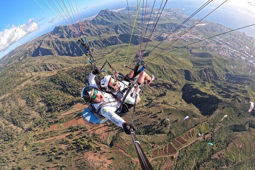 Een persoon paraglide boven een bergachtig landschap met zichtbare valleien en velden. 1