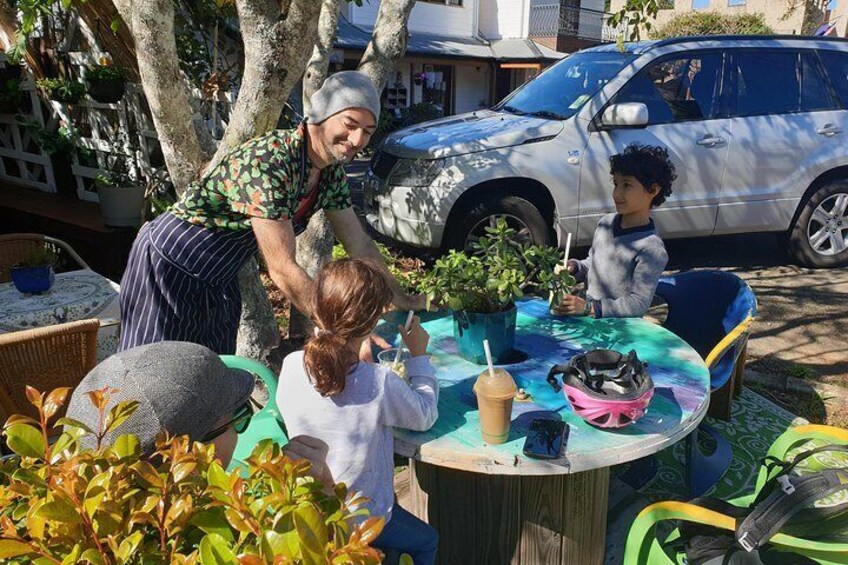 A group of people sitting at a round table outdoors with a car parked nearby. 4