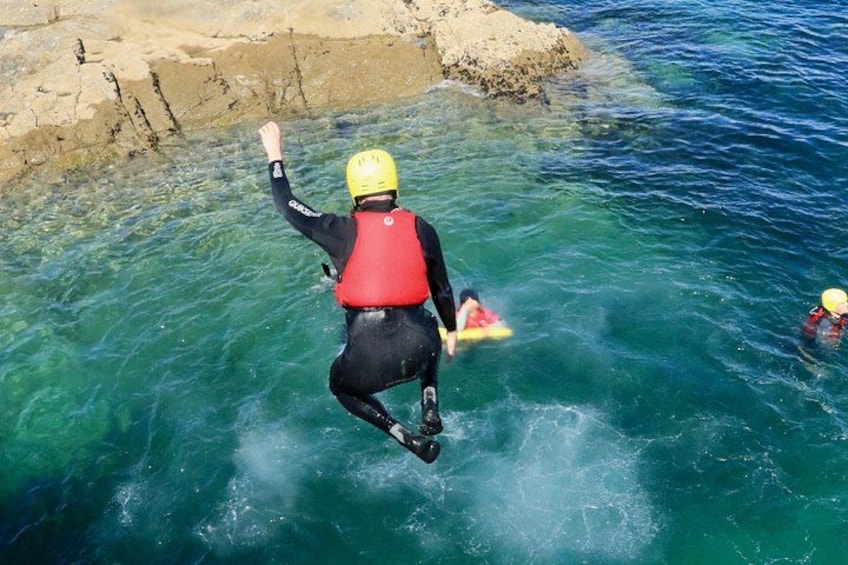 A person diving into clear blue water with a red life jacket and a yellow helmet. 4