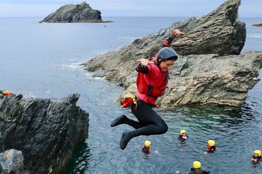 A person jumping off a rocky cliff into the water with several others in the background. 5