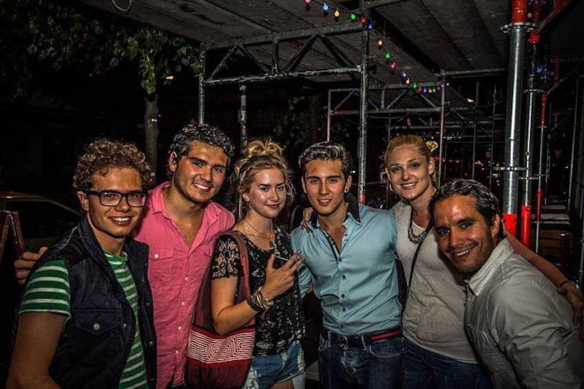 A group of people posing together in an urban setting with metal structures and string lights in the background. 1
