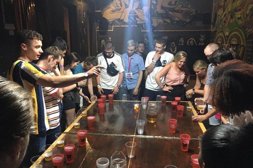 A group of people around a table with red cups and a bottle. 2