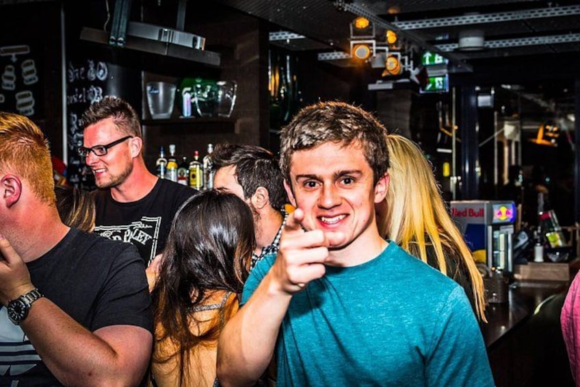 A bar with people socializing, shelves with bottles, and a Red Bull sign. 3