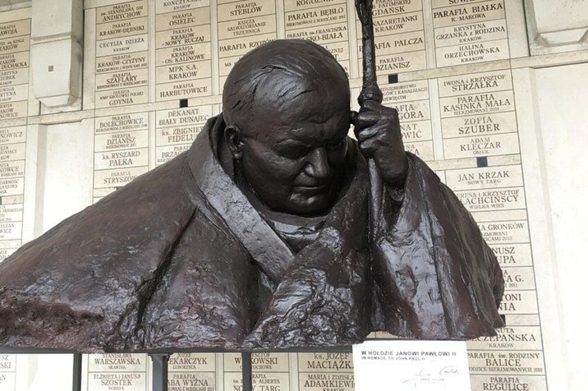 A bronze statue of a man holding a book, with a background of a wall with text. 1