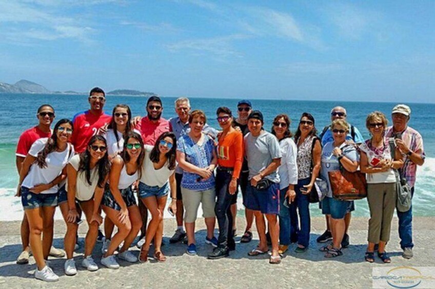 A group of people standing on a concrete surface by the sea, with the ocean and a clear sky in the background. 5