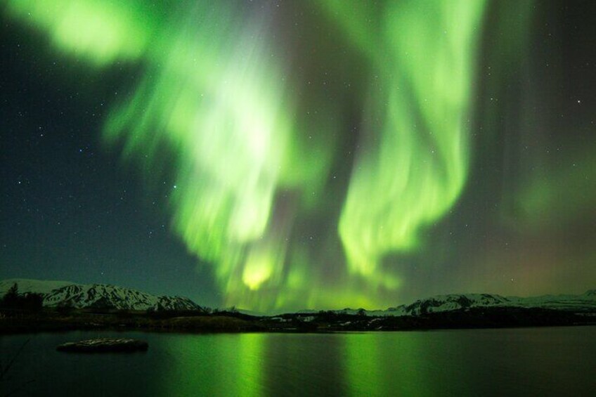 Norrskenet över en stilla sjö med snötäckta berg i bakgrunden. 1