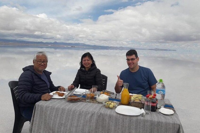 Three people dining at a table with a view of a vast salt flat and distant mountains. 5