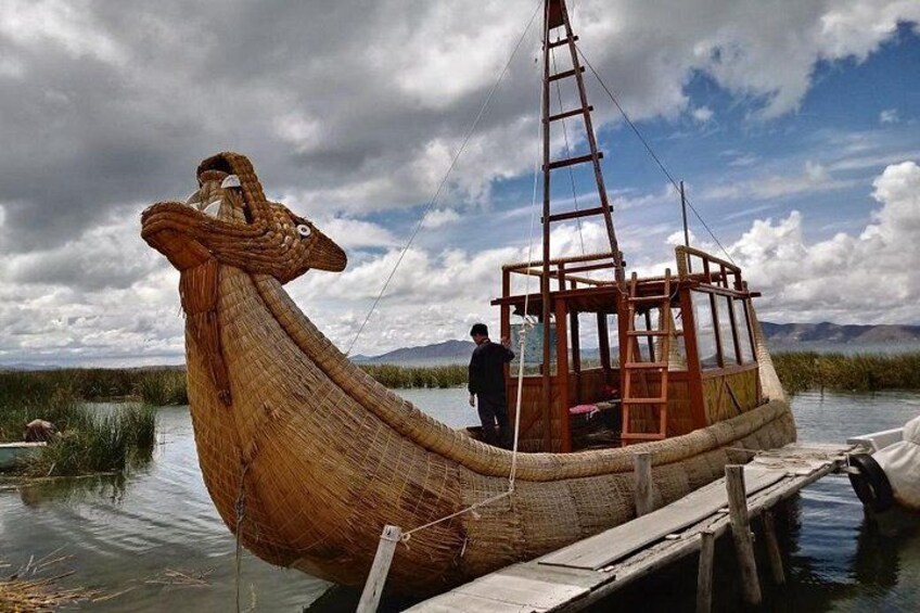 Ein großes hölzernes Boot mit einer Leiter, an einem ruhigen Gewässer gelegen, mit Bergen im Hintergrund. 4