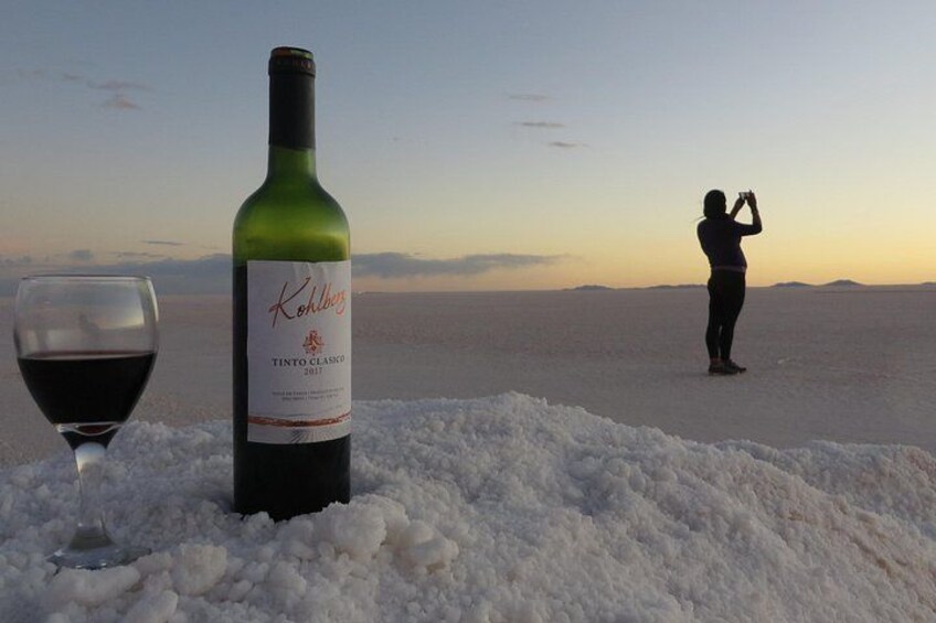 A bottle of wine and a glass on a snowy landscape with a person taking a photo. 2