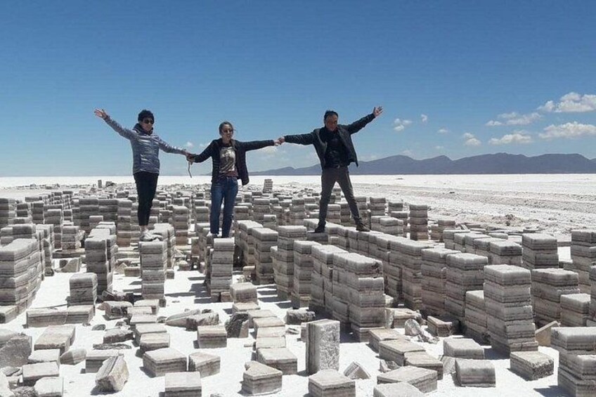Three people standing on stone blocks in a desert landscape with mountains in the background. 5