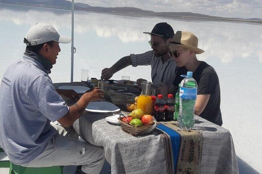 A group of people at a table with food and drinks, overlooking a body of water. 3