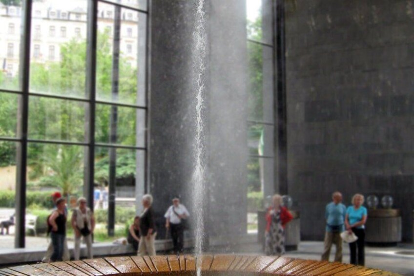 Une fontaine avec des jets d’eau, entourée d’une place où les gens se promènent et se tiennent debout. 2