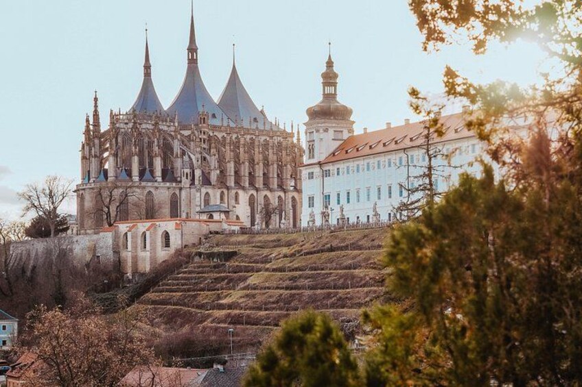 A historic cathedral with three spires, a bell tower, and a building with a red roof. 1