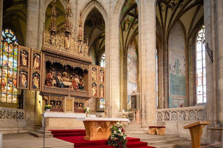 An ornate church interior with a central altar, stained glass windows, and a red carpet. 3