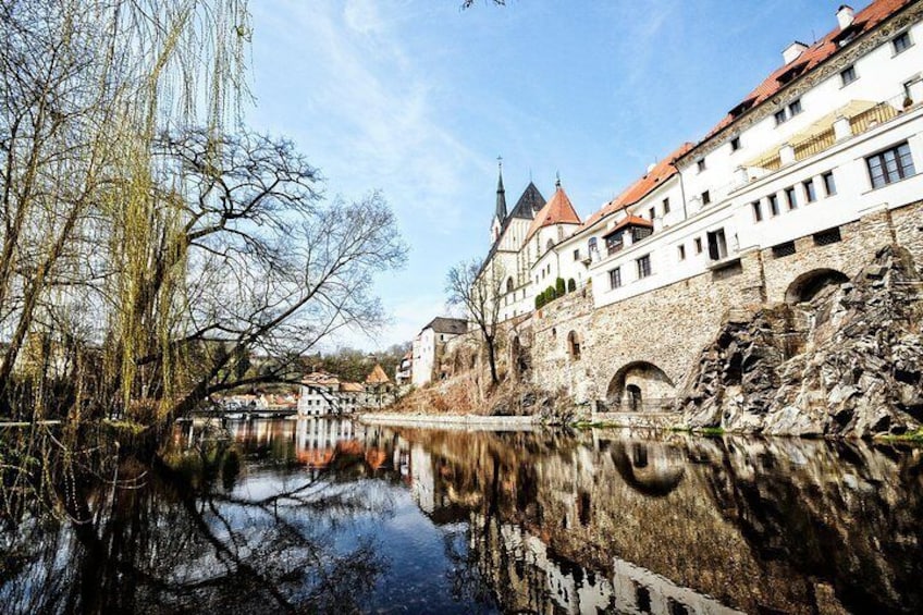 A historic building with a stone facade and red-tiled roof, reflecting in a calm river. 4