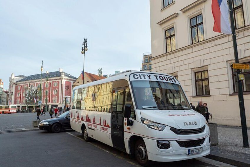 Un autobús turístico blanco estacionado en una calle con edificios y una bandera al fondo. 3