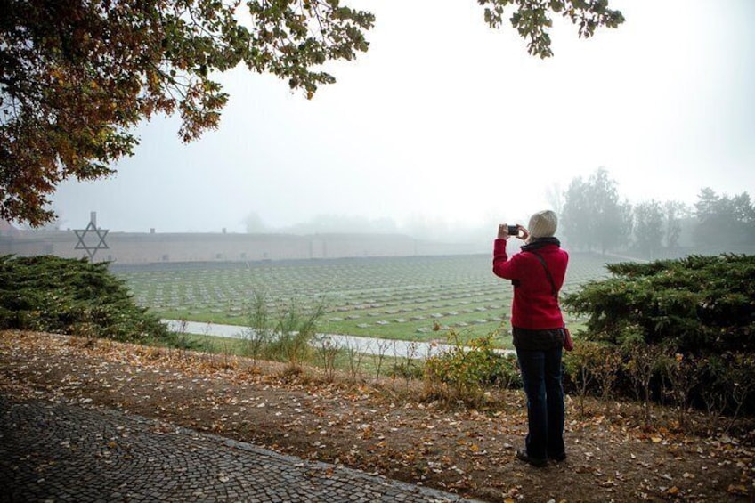 A person in a red jacket taking a photo of a field with a Star of David in the distance. 4