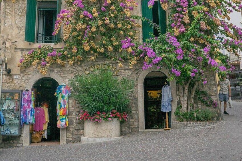 Un edificio in pietra con persiane verdi, un muro ricoperto di fiori e una strada acciottolata. 2