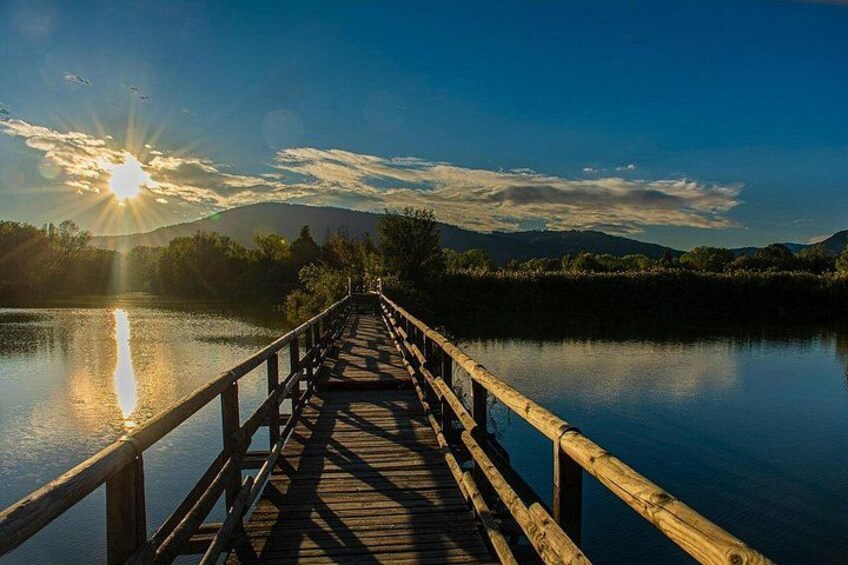 Un ponte di legno sopra acque calme con un tramonto sullo sfondo. 3