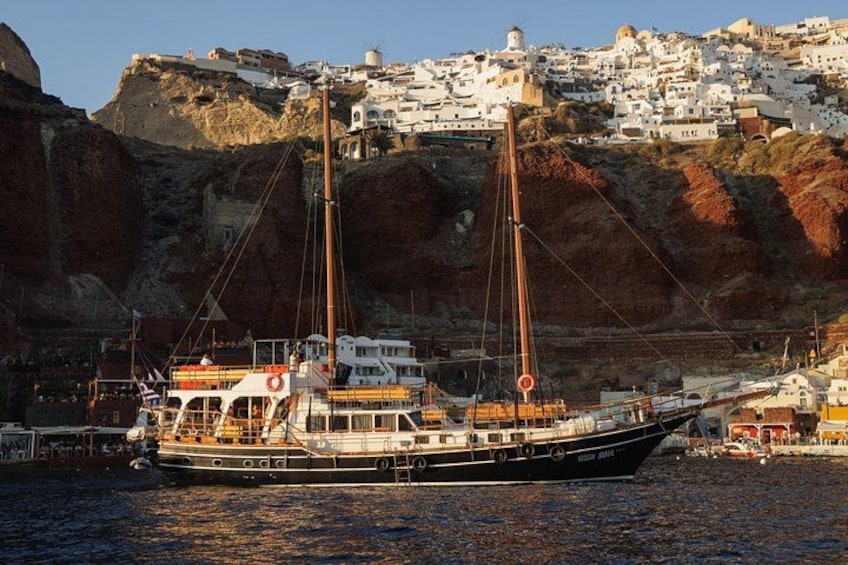 A sailing boat docked at a harbor with white buildings on a hillside in the background. 1