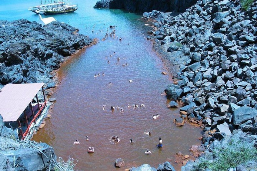 A rocky shoreline with a boat in the background and people swimming in the water. 4