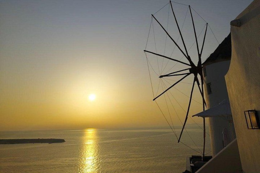 A sunset over a calm sea, a windmill, and a building with a white facade. 3