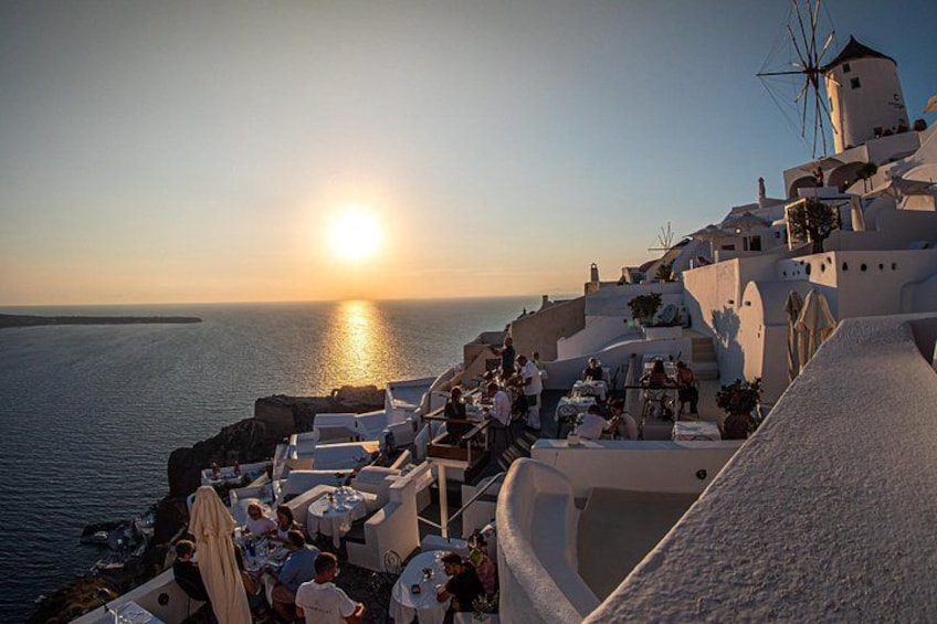 A coastal town with white buildings, a windmill, and a sunset over the sea. 5