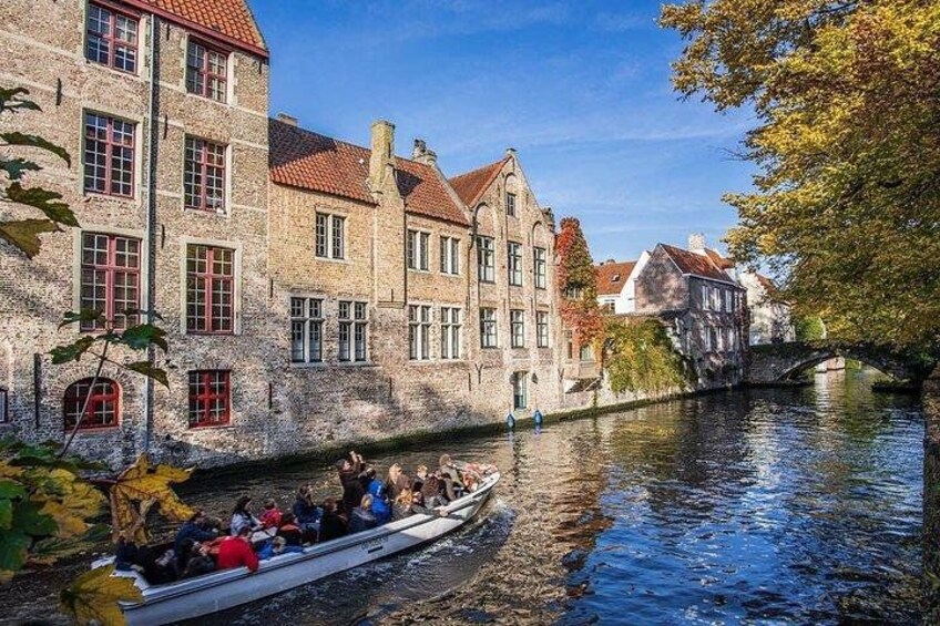 Un canal con un bote que transporta pasajeros, edificios históricos y un árbol con hojas otoñales. 4