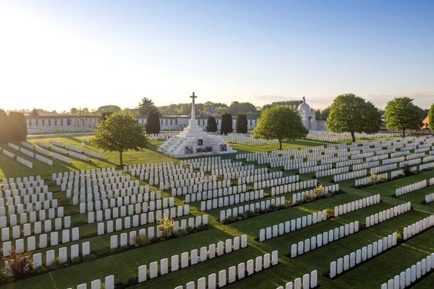 A cemetery with numerous white headstones arranged in orderly rows, a central monument, and a building with a dome in the background. 2