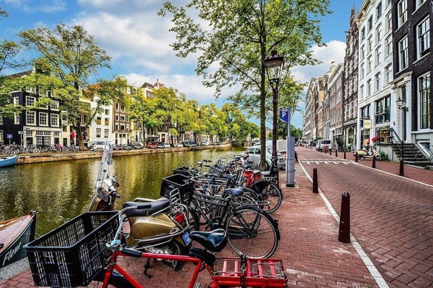 Un canal con bicicletas estacionadas a lo largo de la orilla, una hilera de edificios y un cielo despejado. 5