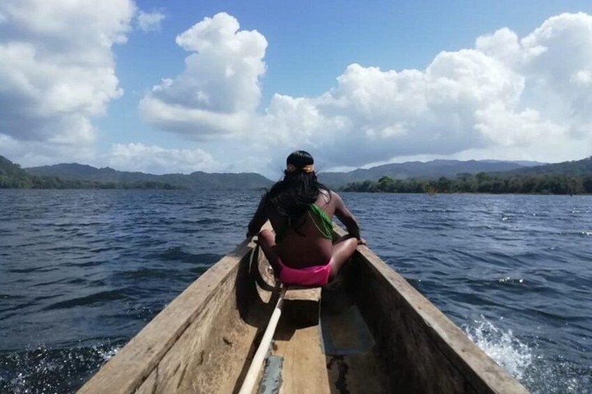 A person rowing a wooden boat on a calm body of water with mountains in the background. 5