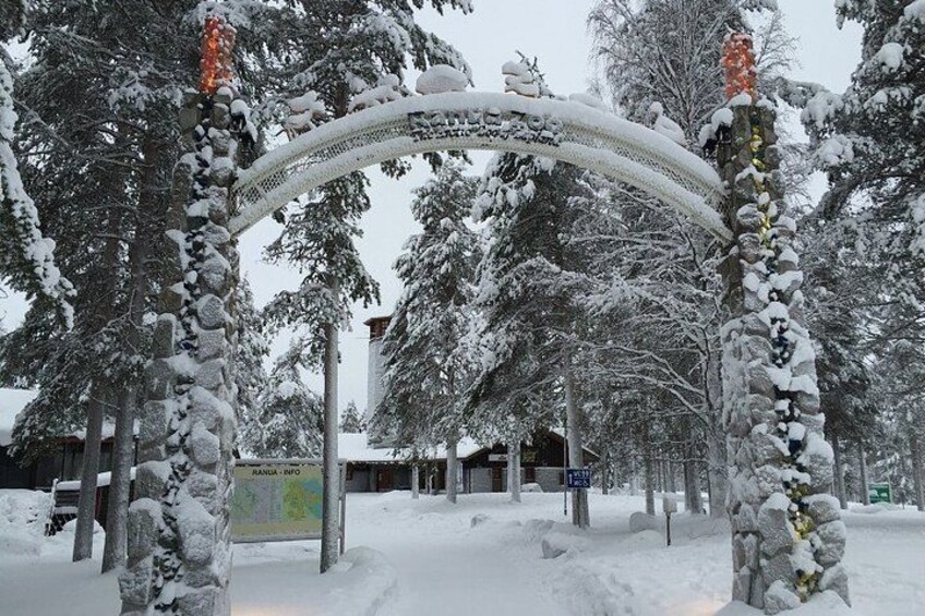 A snow-covered archway with a sign, surrounded by trees and buildings. 2