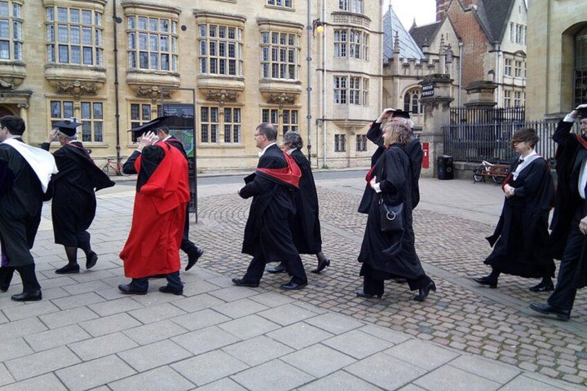 Graduates in academic regalia walking on a cobblestone street. 5