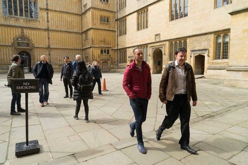 A group of people walking in a courtyard with a 'NO SMOKING' sign. 2