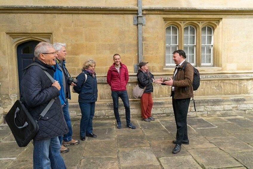 A group of people standing on a stone pavement in front of a building with arched windows and a door. 4