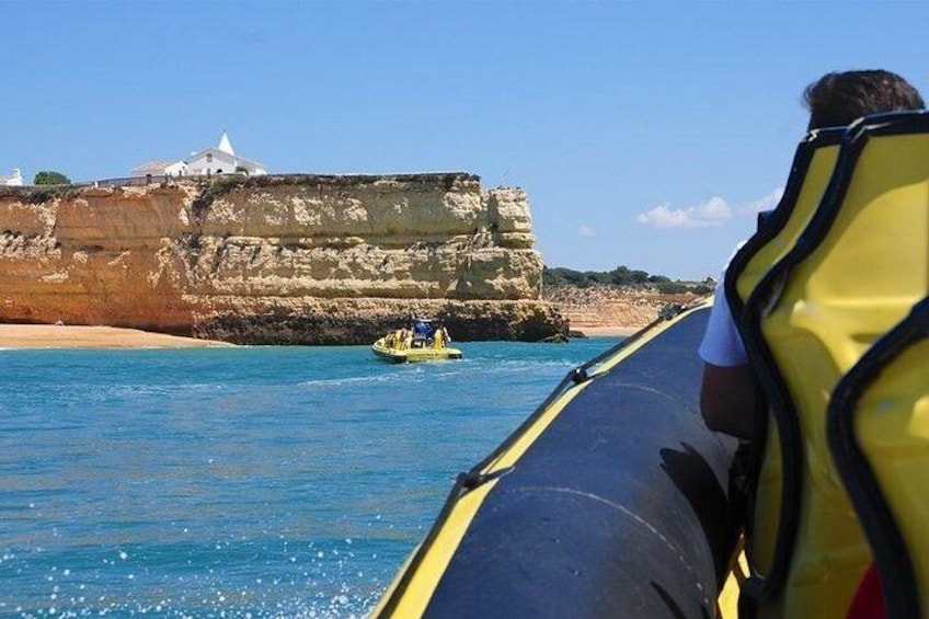 A boat with a person wearing a life jacket, a rocky coastline, and a small yellow boat in the water. 2
