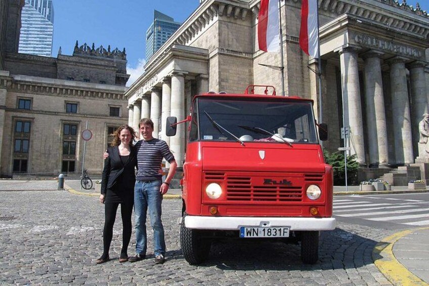 A red vintage car parked in front of a historic building with columns and flags. 1
