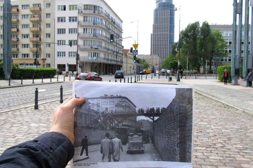 Una persona sostiene una fotografía antigua que muestra una calle con edificios y un puente. 4