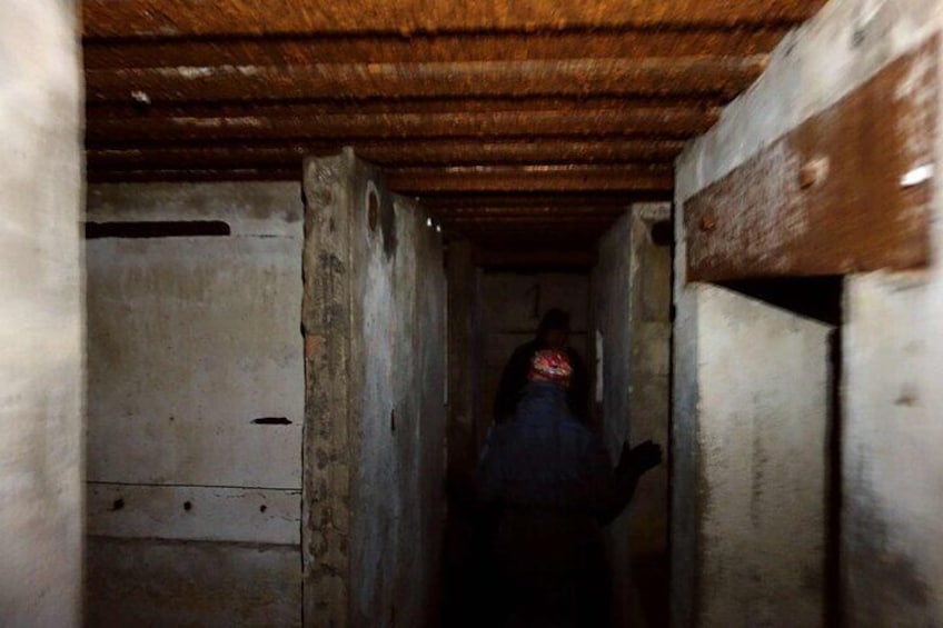 Un corridoio stretto e poco illuminato, con pareti in cemento e soffitto in legno. 1