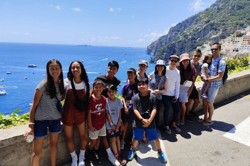 Un gruppo di persone su una strada costiera con vista sul mare e un paesaggio montuoso. 1