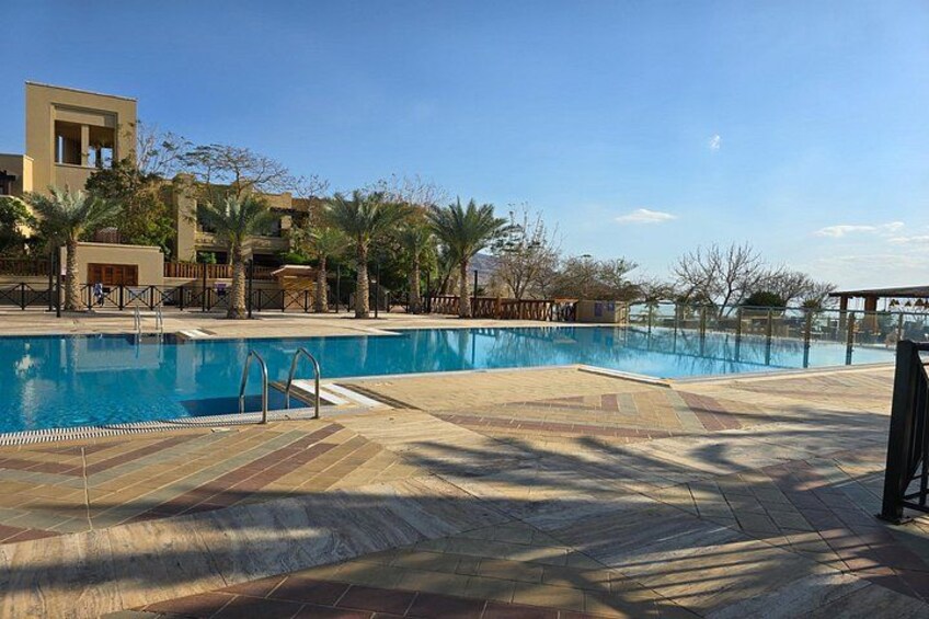 A swimming pool with a wooden deck, palm trees, and a building in the background. 3