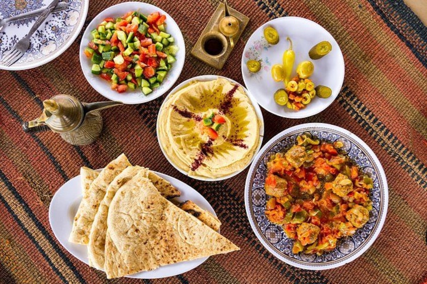 A table with various dishes including hummus, a vegetable salad, a plate of flatbread, and a bowl of stew. 2