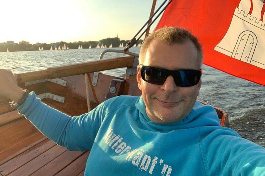 A person on a boat with a red flag, water, and a distant shoreline with buildings. 2